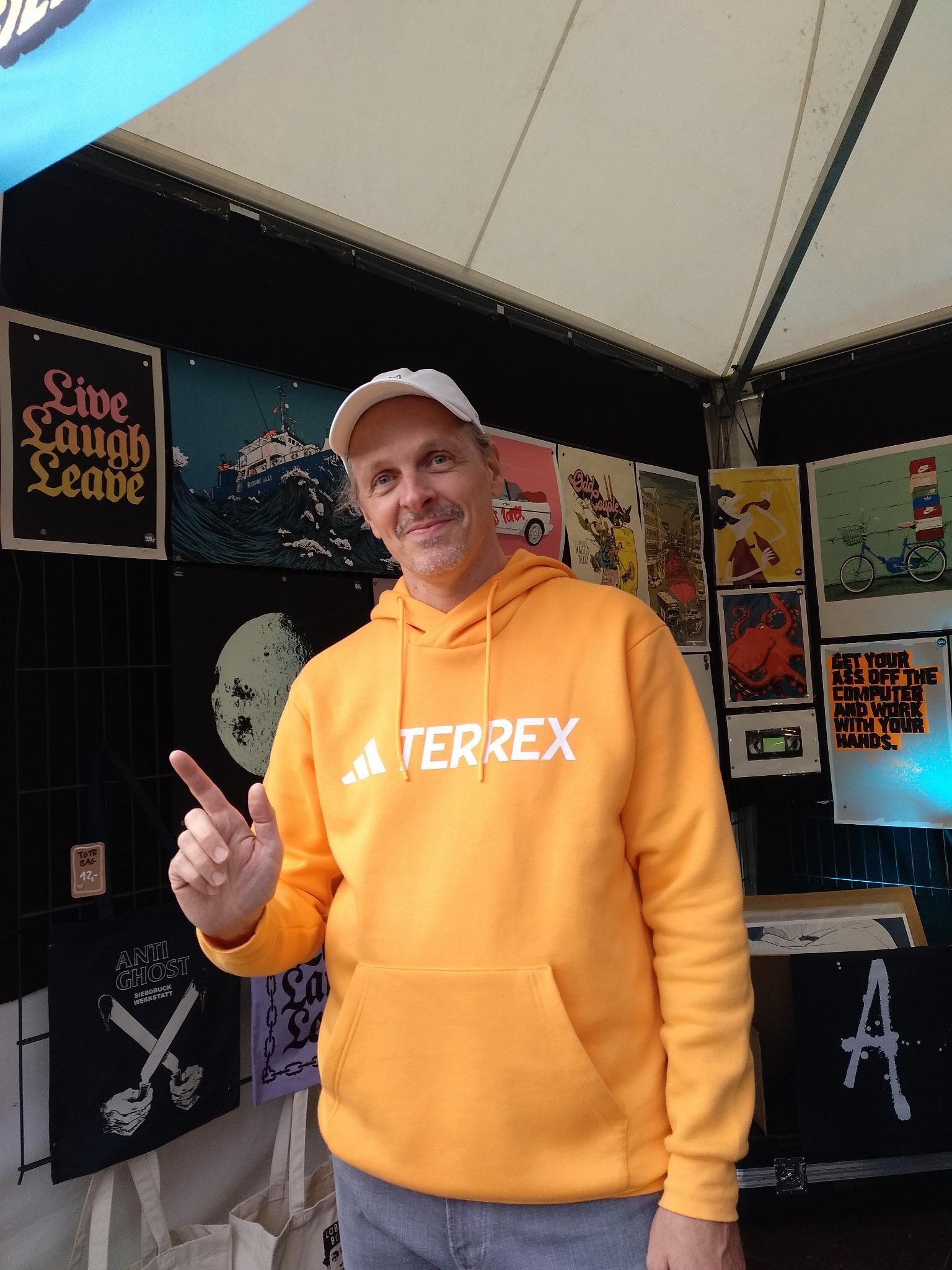 Loopuz in an orange jacket and white cap at an outdoor art stall